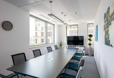 Professional meeting room with a dark grey table, teal chairs, and a large window providing natural light.