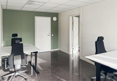 Bright office space with two desks, black ergonomic chairs, and a sage green feature wall.