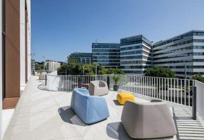 Sunlit outdoor terrace with colorful modern seating overlooking city office buildings.