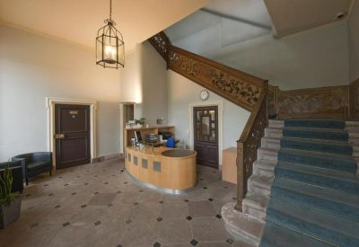 Elegant reception hall featuring a curved wooden desk and a grand staircase with ornate carvings.