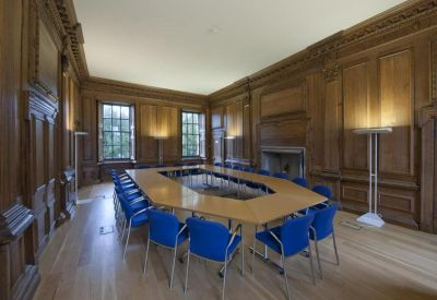 Stately boardroom with dark wood paneling, a large hollow square table, and blue chairs.