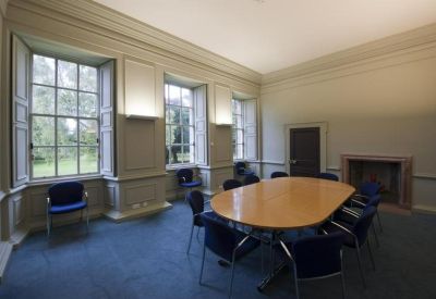Bright meeting room with light-colored walls, large windows, and an oval wooden table with blue chairs.
