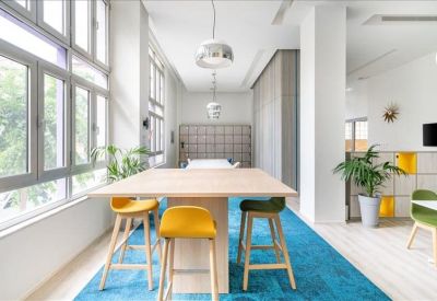 Breakout area with high wooden table, yellow stools, and a bright blue rug.