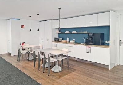 Modern communal kitchen and dining area with white cabinetry, a coffee machine, and wooden floors.