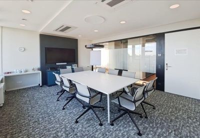 Meeting room with a white table, grey ergonomic chairs, and a large wall-mounted monitor.