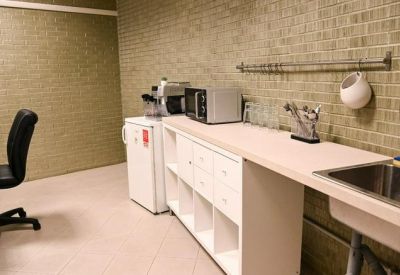 Breakroom kitchen area with a white sideboard, microwave, and sink against a brick wall.