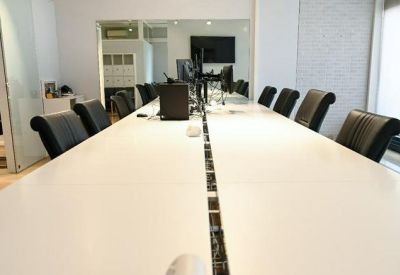 Long white communal workstation with ergonomic black chairs in a bright office.