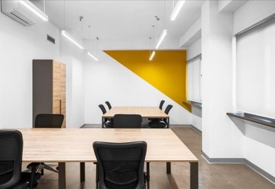 Open-plan coworking area with light wood tables and a yellow geometric accent wall.