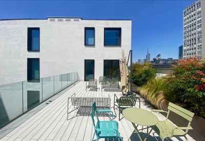Bright office space with people working at a long wooden table under industrial piping.