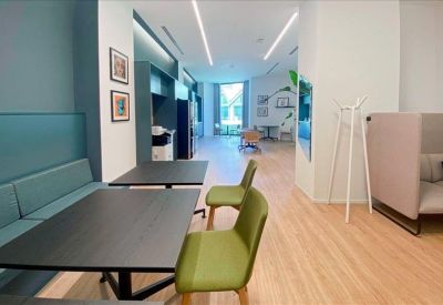 Communal breakout area with black dining tables, green chairs, and a turquoise booth.