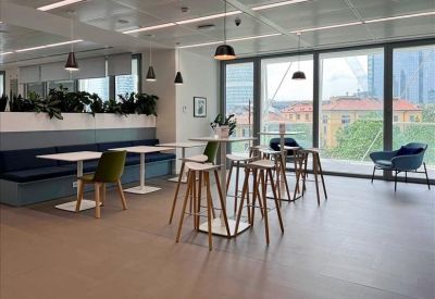 Contemporary breakout area with high tables, wooden stools, and large windows with city views.