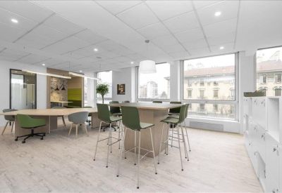 Open-plan coworking space with wooden floors, various seating, and large windows.