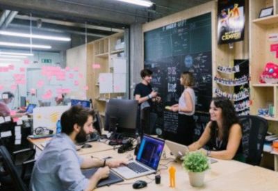 Open-plan coworking area with a large chalkboard and people working at wooden desks.