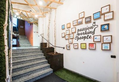 Modern reception entrance with a branded wall, decorative wood ceiling, and a grey stone staircase.
