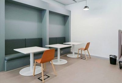 Casual dining or meeting area with white tables, orange chairs, and built-in teal wall seating.