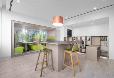 Communal breakout area with a high table, green stools, and a designer copper pendant light.