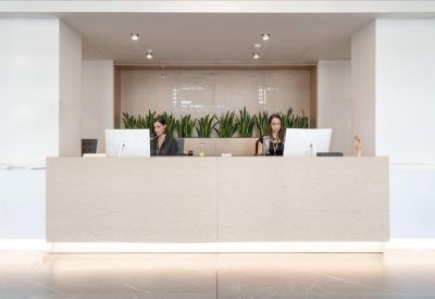Minimalist white reception desk with two staff members and green plants.