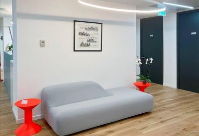 Bright waiting area with wood-effect flooring, a grey couch, and vibrant red side tables.