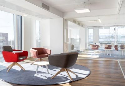 Sunlit breakout lounge with contemporary grey and red seating on a wooden floor.