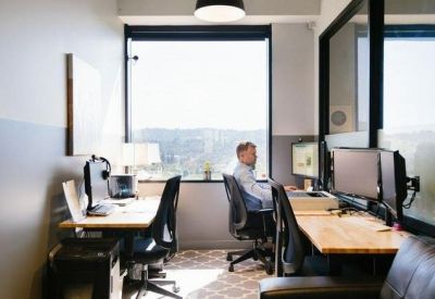 Private glass-walled office suite with multiple computer monitors and city views.