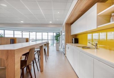 Modern office kitchen with long wooden breakfast bar and bright yellow backsplash.