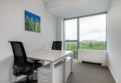 Private two-person office with white desks and large window overlooking trees.