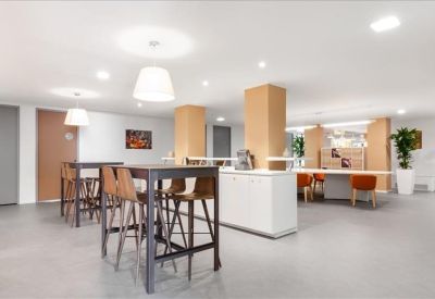 Spacious breakout area with high tables, wooden stools, and white cabinetry.