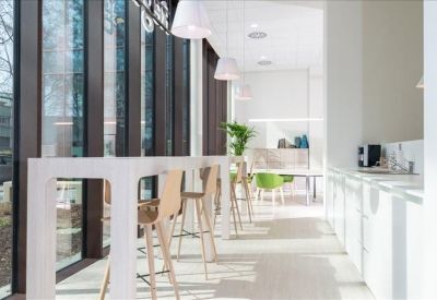 Modern break area featuring high white tables and light wood stools by a window.