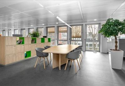Open-plan workspace with wooden storage units and grey chairs around a shared table.