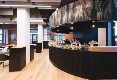Spacious cafe and breakout area with a curved black service counter and wooden flooring.