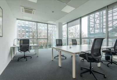 Bright open-plan office with white desks, ergonomic black chairs, and large windows.