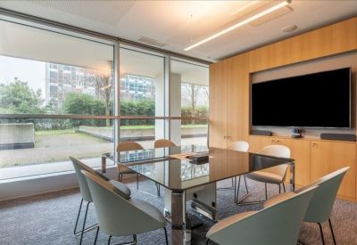 Modern conference room featuring a large table, grey chairs, and a wall-mounted screen.