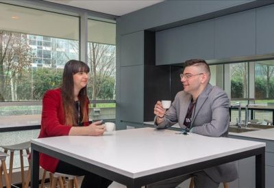 Two people having coffee and a discussion at a high table in a modern breakout room.