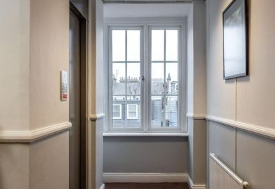 Neutral toned office corridor with carpeted flooring, a radiator, and large windows at the end.