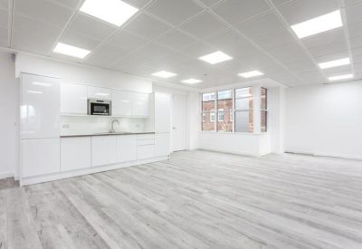 Minimalist communal kitchen and breakout area with white cabinetry and grey wood flooring.