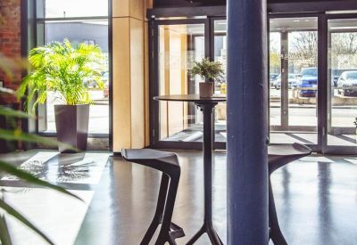 Sunlit lobby area with a tall blue pillar and high-top seating near the glass entrance.