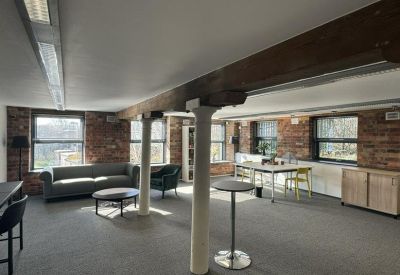 Open-plan office space featuring exposed brick walls, timber beams, and various seating areas.