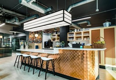 Modern office kitchen featuring a copper-textured island bar and industrial ceiling pipes.