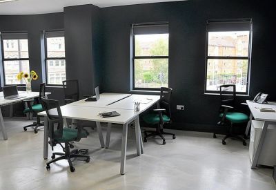 Open-plan office space with white desks, ergonomic green chairs, and dark grey walls.