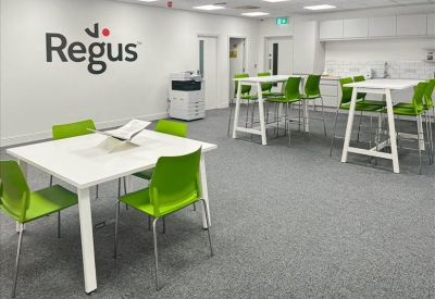 Bright communal kitchen and breakout area with high-top tables and green chairs.