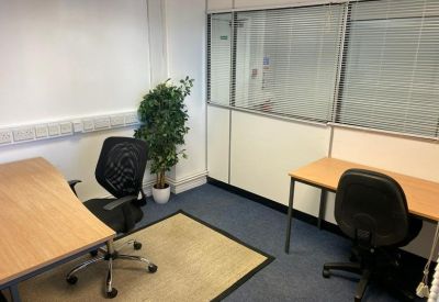Two-person office suite with light wood desks, black chairs, and a small area rug over blue carpet.