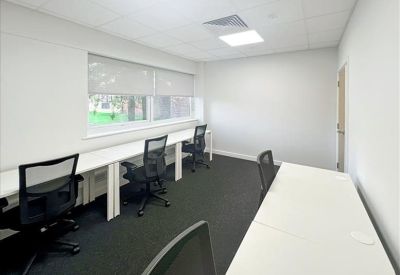 Bright open-plan office with white desks and black mesh chairs near a large window.