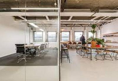 Glass-walled meeting room adjacent to a bright communal breakout area with potted plants.