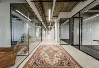Modern office corridor with glass walls, exposed concrete ceilings, and a decorative Persian rug.