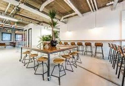 Spacious communal coworking space with industrial ceilings and warm wood tables.