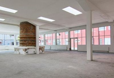 Large empty industrial loft space with a central brick pillar and large windows.