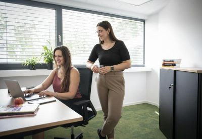 Sunlit office space with two women collaborating at a desk by a window.