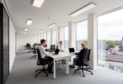 Bright open-plan office with desks facing large windows and city views.