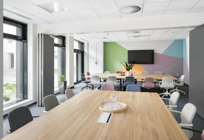 Spacious meeting room with large wooden tables, colorful chairs, and a wall-mounted TV.