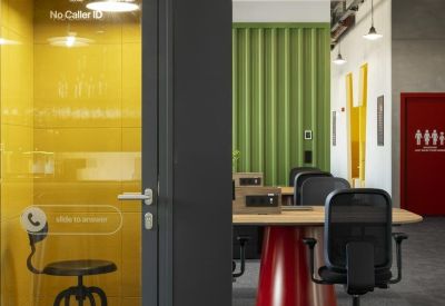 A private yellow phone booth with a tall stool and glass door.
